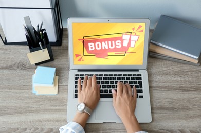 Bonus gaining. Woman using laptop at wooden table, above view. Illustration of gift box and word on device screen