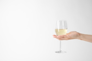 Photo of Woman holding glass of expensive white wine on light background