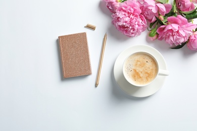 Beautiful peony flowers, notebook and cup of coffee on white background, top view