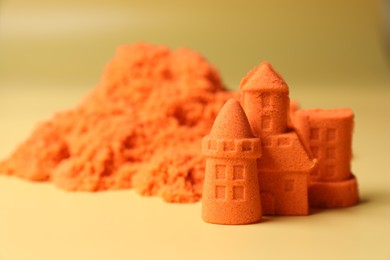 Photo of Castle figures made of orange kinetic sand on beige background, closeup. Space for text