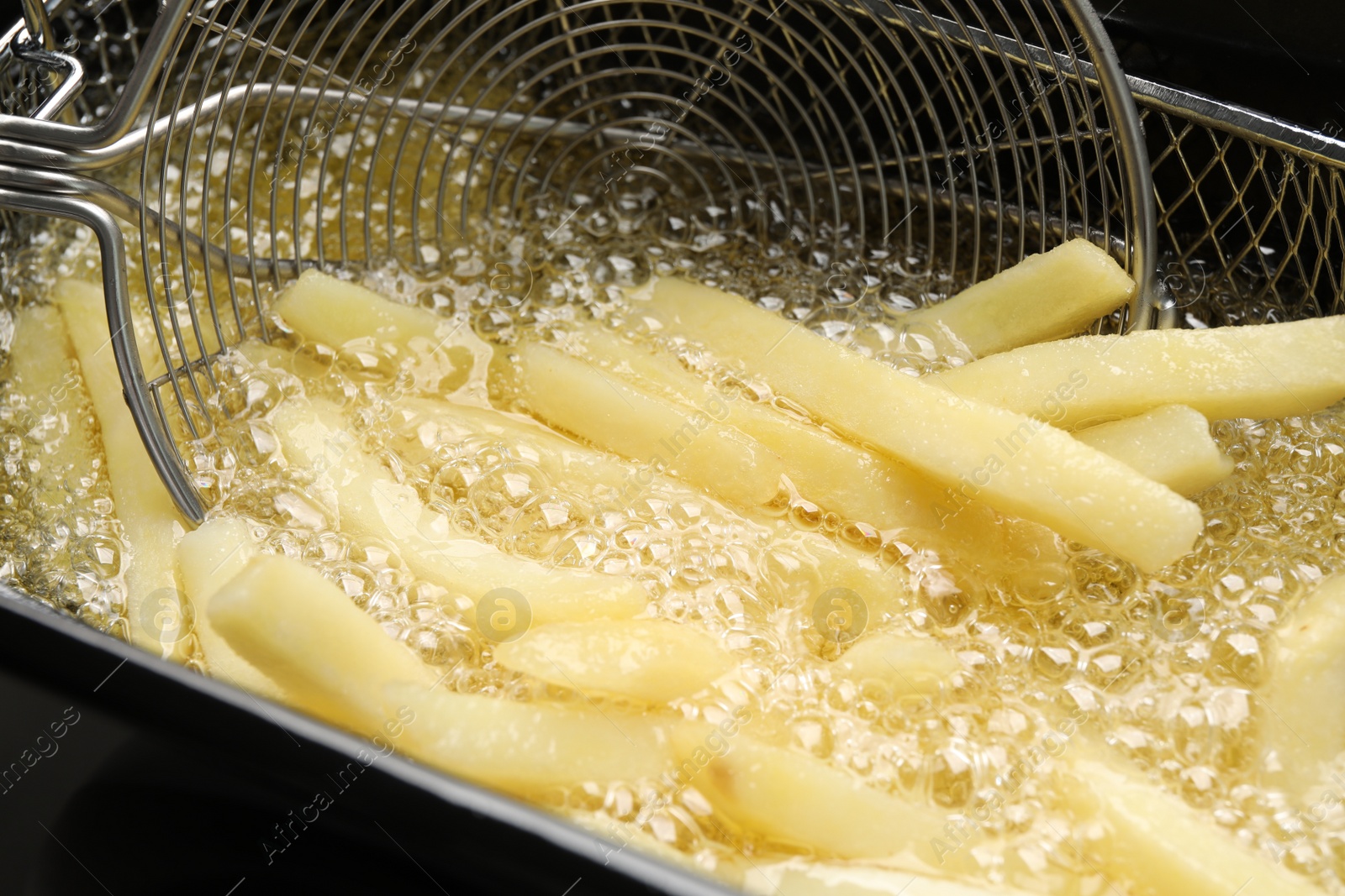 Photo of Cooking delicious french fries in hot oil, closeup