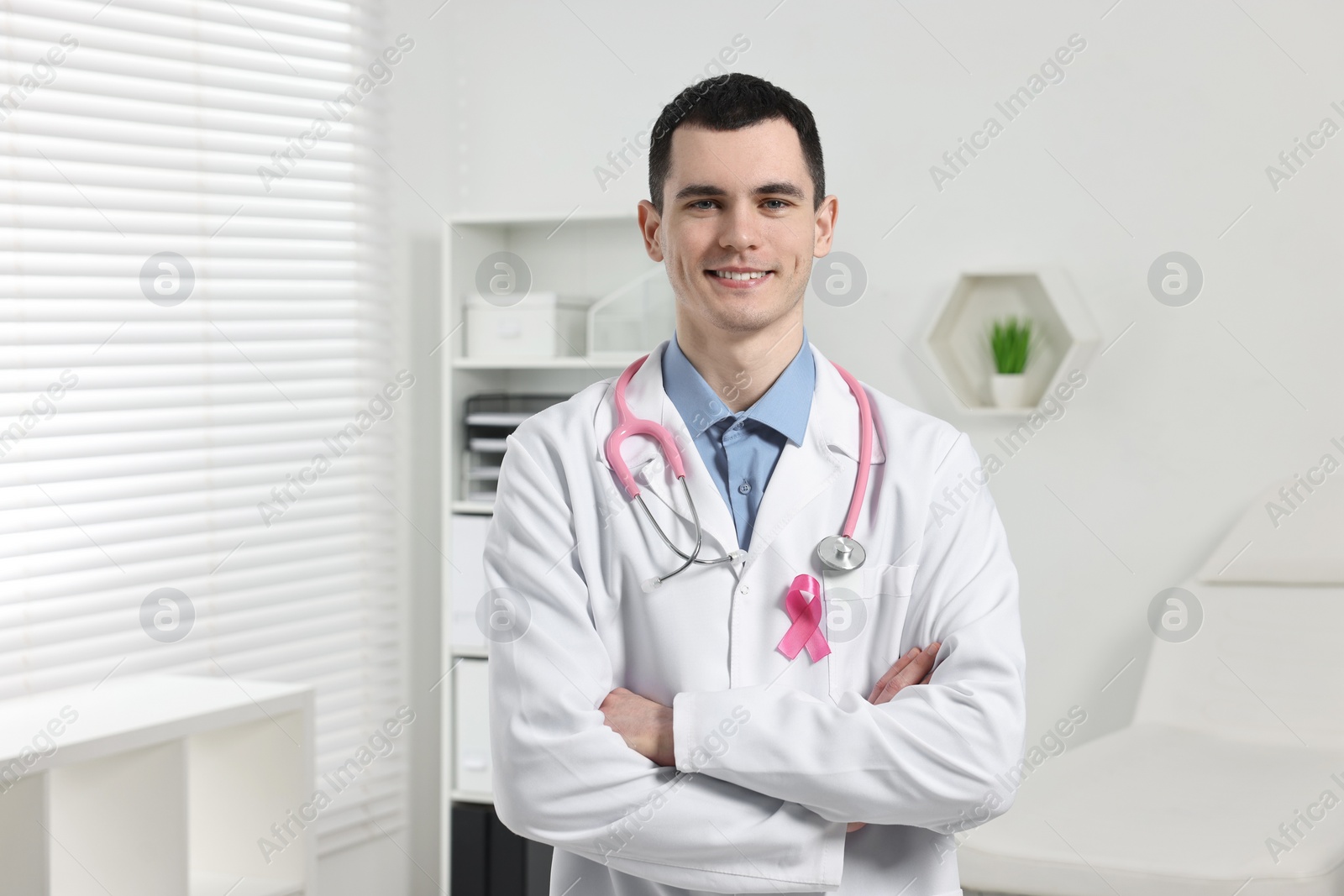 Photo of Portrait of smiling mammologist with pink ribbon and stethoscope in hospital. Breast cancer awareness