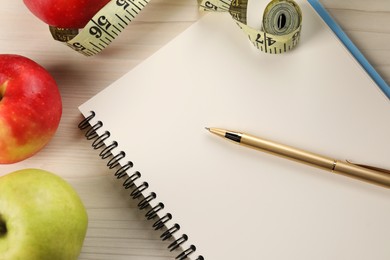 Photo of Healthy diet. Fresh apples, measuring tape, notebook and pen on light wooden table, flat lay