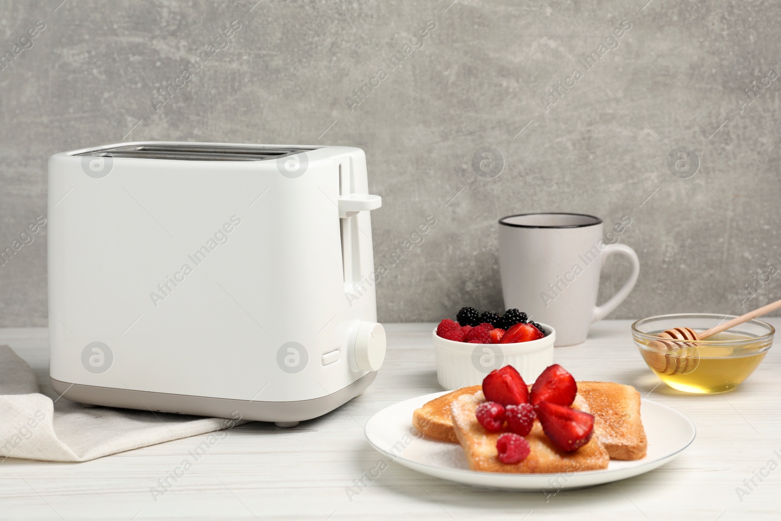 Photo of Modern toaster, bread with fresh berries, honey and cup on white wooden table