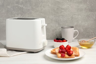 Modern toaster, bread with fresh berries, honey and cup on white wooden table