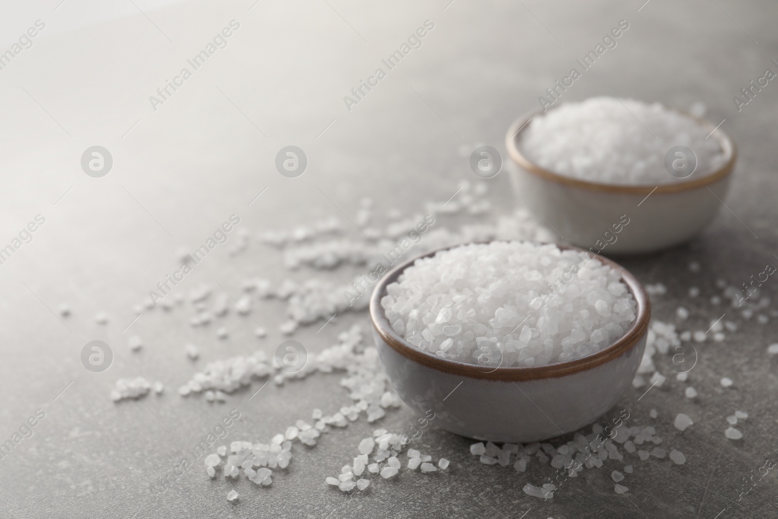 Photo of Bowls of natural sea salt on grey table, closeup. Space for text