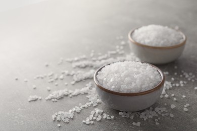 Bowls of natural sea salt on grey table, closeup. Space for text
