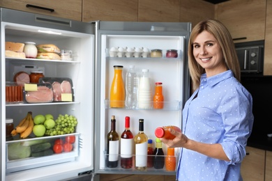 Woman with bottle of juice near refrigerator in kitchen