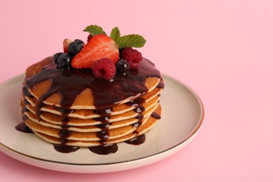 Photo of Stack of tasty pancakes with fresh berries, chocolate sauce and mint on pink background, closeup. Space for text