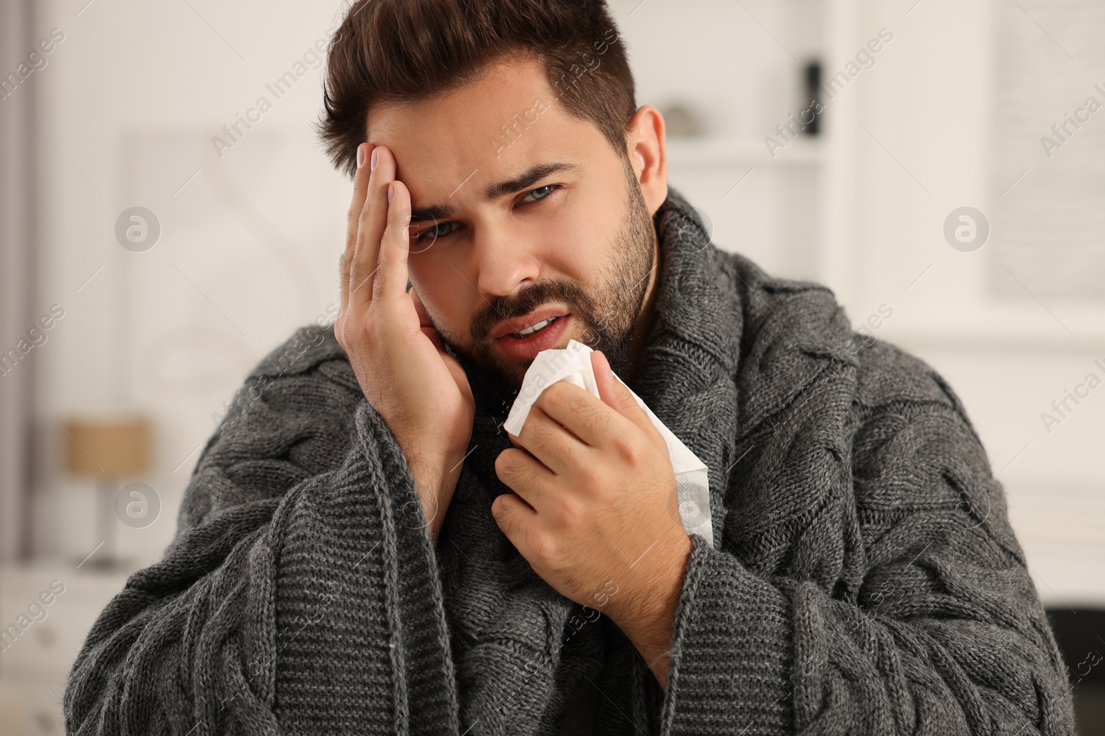 Photo of Sick man wrapped in blanket with tissue at home. Cold symptoms