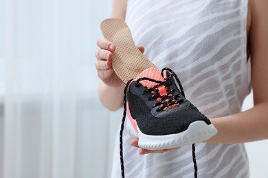 Woman putting orthopedic insole into shoe indoors, closeup and space for text. Foot care