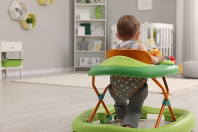 Photo of Cute baby making first steps with toy walker at home, back view. Space for text
