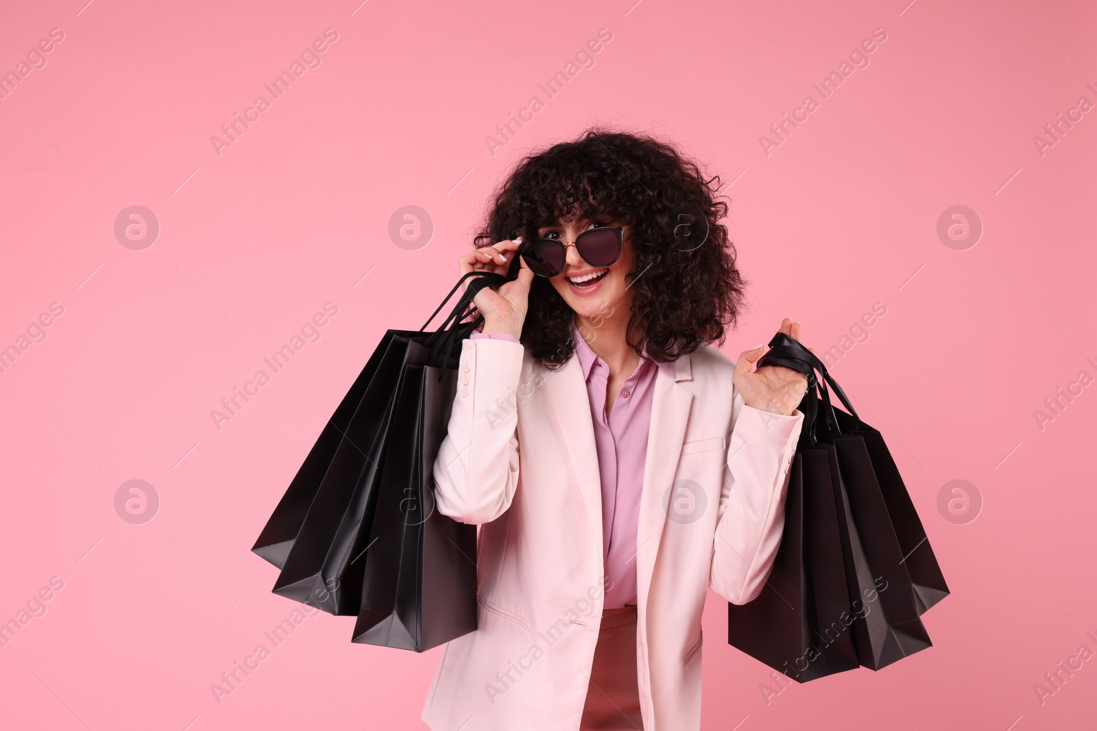 Photo of Happy young woman with shopping bags and stylish sunglasses on pink background