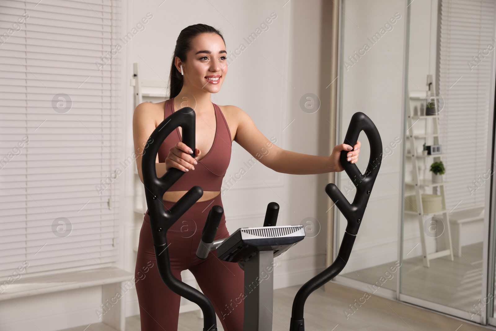 Photo of Happy young woman training on elliptical machine at home