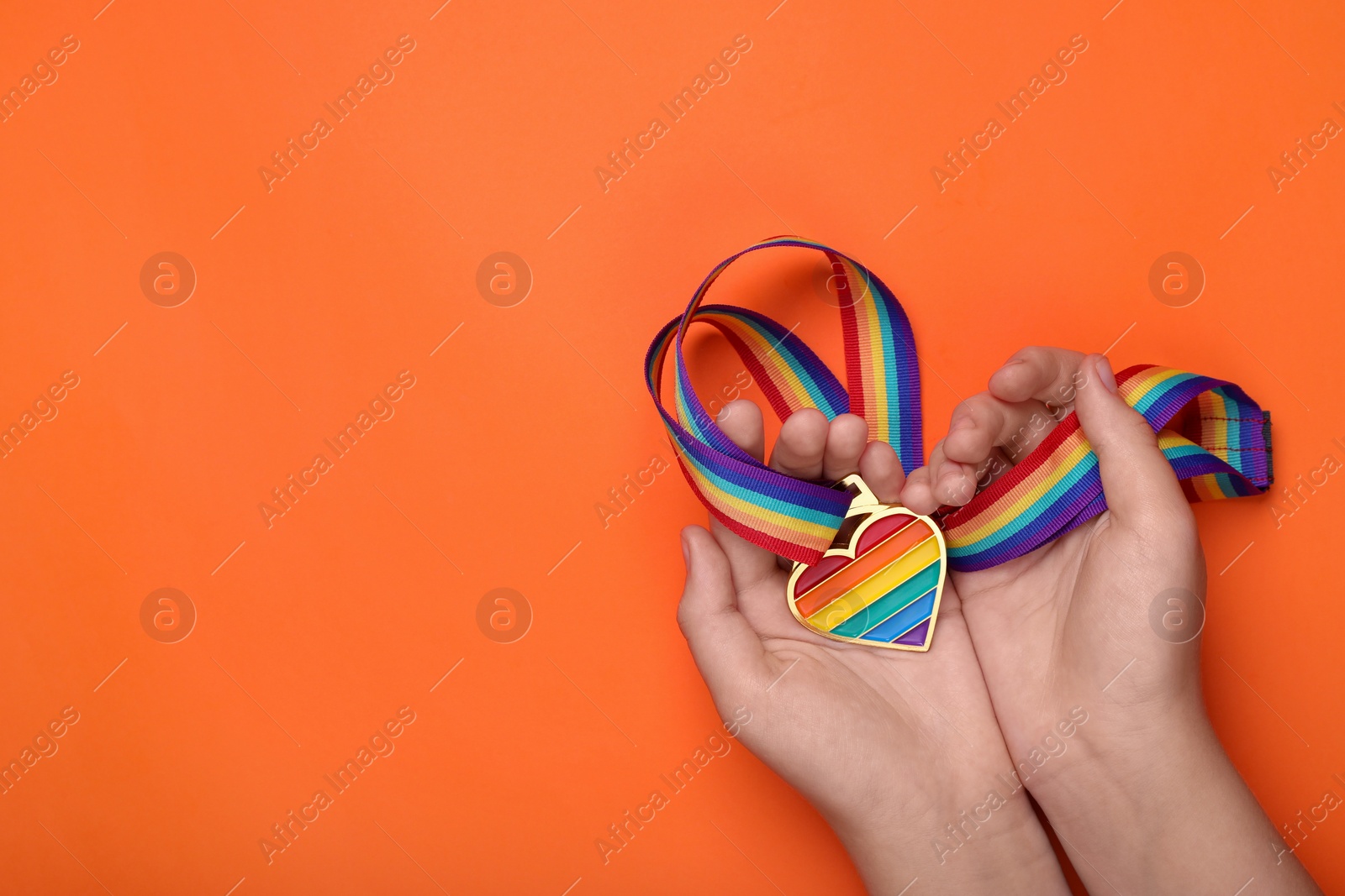 Photo of Woman holding rainbow ribbon with heart shaped pendant on orange background, top view and space for text. LGBT pride