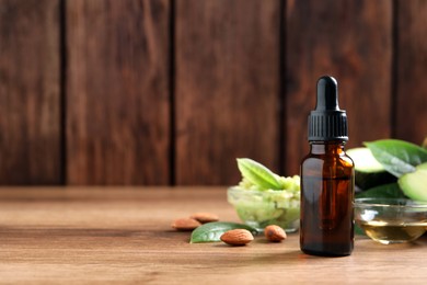 Bottle of essential oil, fresh avocado and almonds on wooden table, space for text