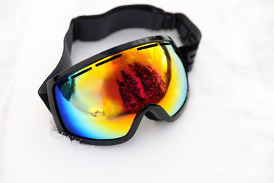 Photo of Stylish ski goggles on snow outdoors. Winter sport equipment