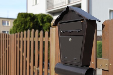 Photo of Beautiful house shaped mailbox with newspaper holder on wooden fence outdoors, space for text