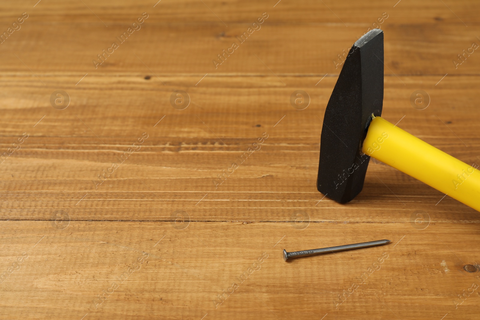 Photo of New hammer and metal nail on wooden table, closeup. Space for text