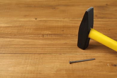 Photo of New hammer and metal nail on wooden table, closeup. Space for text