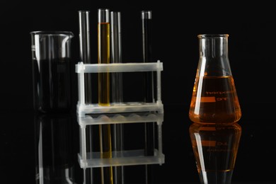 Laboratory glassware with different types of oil on black background, closeup