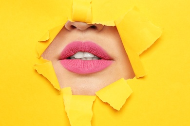 Lips of young woman with beautiful lipstick visible through hole in color paper