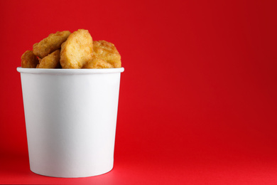 Photo of Bucket with delicious chicken nuggets on red background. Space for text