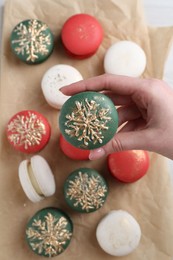 Photo of Woman with decorated Christmas macaron at table, top view