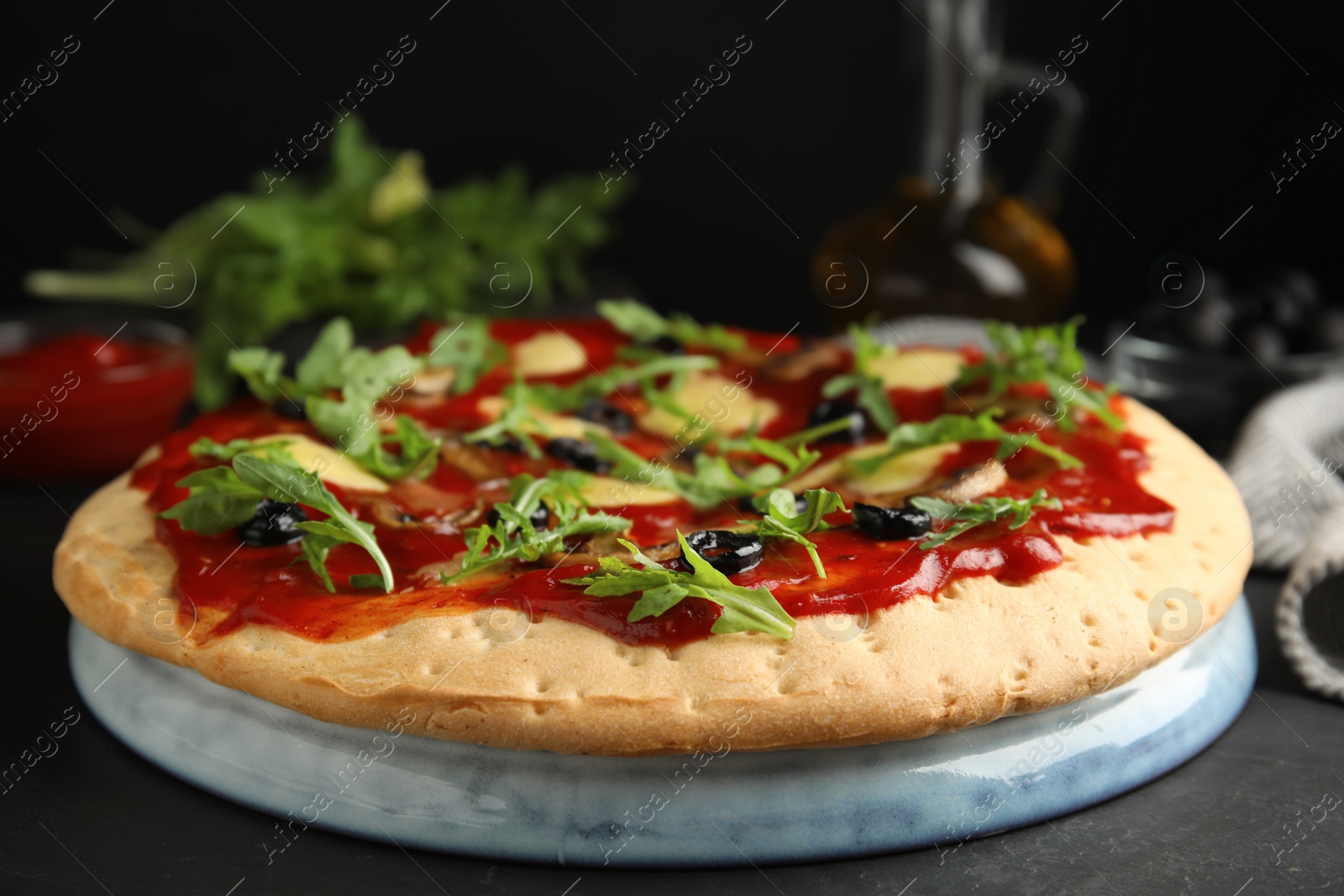 Photo of Pita pizza with cheese, olives, mushrooms and arugula on black table, closeup