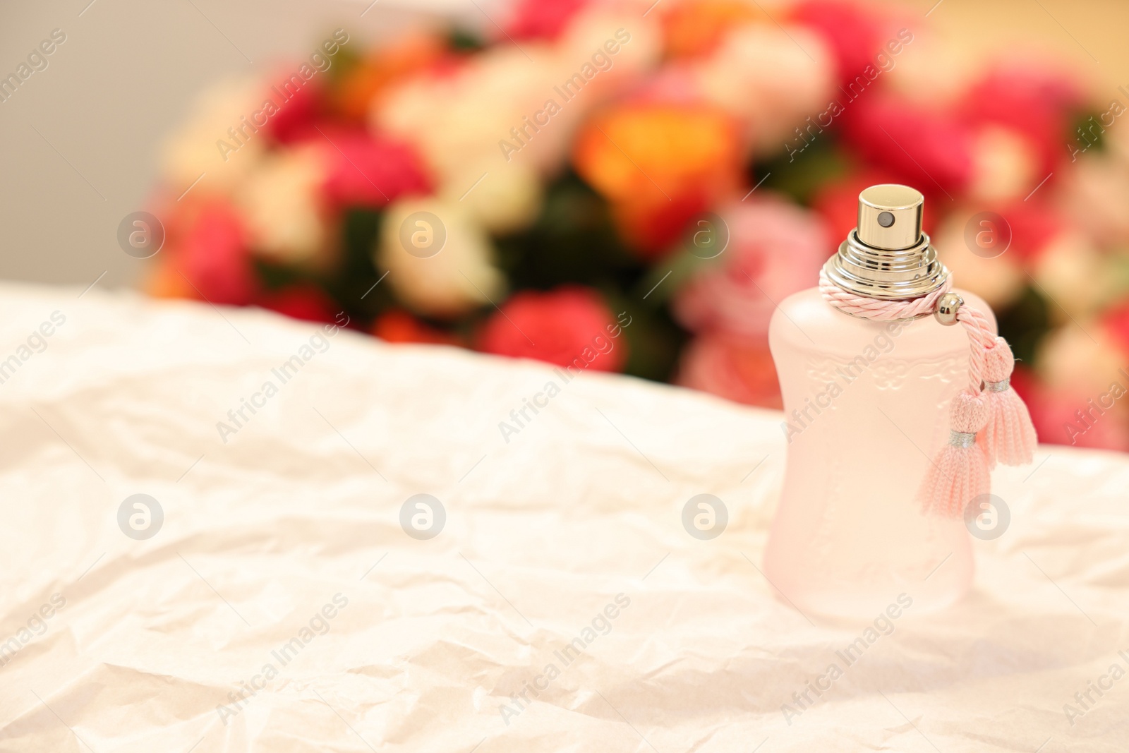 Photo of Bottle of perfume on crumpled paper against beautiful roses. Space for text