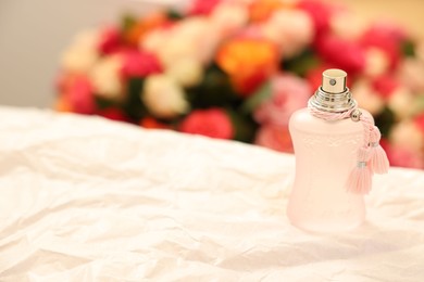 Photo of Bottle of perfume on crumpled paper against beautiful roses. Space for text