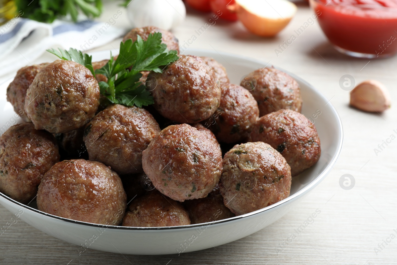 Photo of Tasty cooked meatballs with parsley on white wooden table, closeup