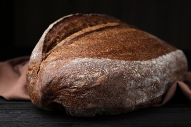 Photo of Loaf of tasty rye sodawater bread on black wooden table, closeup