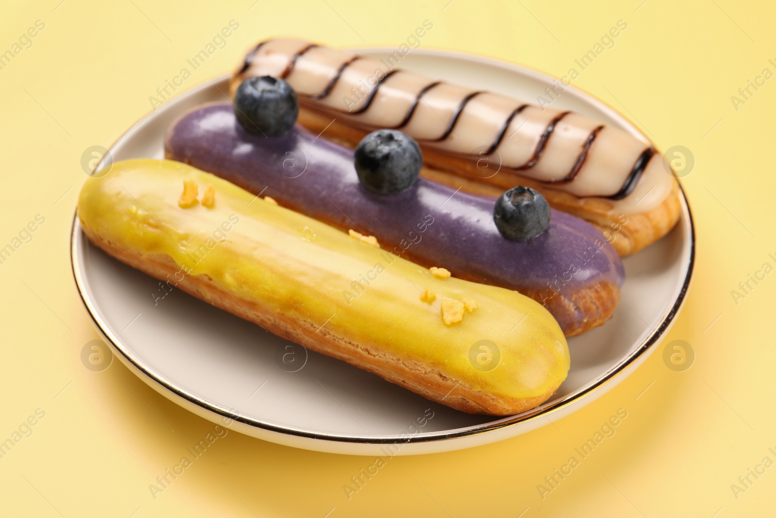 Photo of Delicious eclairs covered with glaze on yellow background