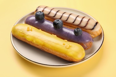 Delicious eclairs covered with glaze on yellow background