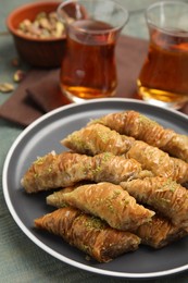 Photo of Delicious baklava with pistachios and hot tea on light blue wooden table
