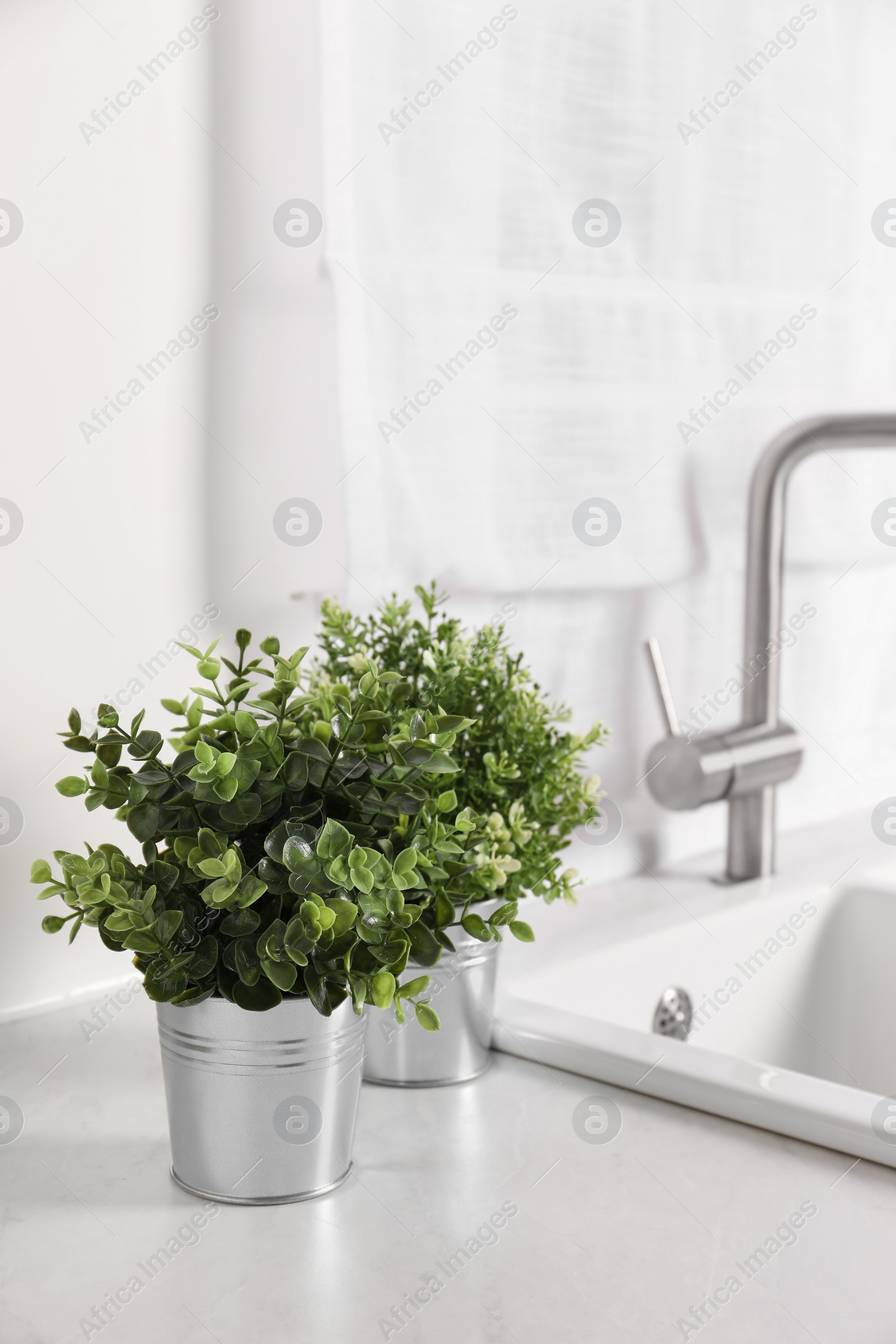 Photo of Artificial potted herbs on white marble countertop near sink in kitchen. Home decor