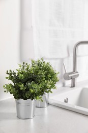 Artificial potted herbs on white marble countertop near sink in kitchen. Home decor
