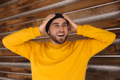 Photo of Young man wearing warm clothes near wooden wall. Winter vacation
