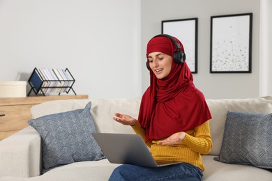 Photo of Muslim woman using video chat on laptop at couch in room
