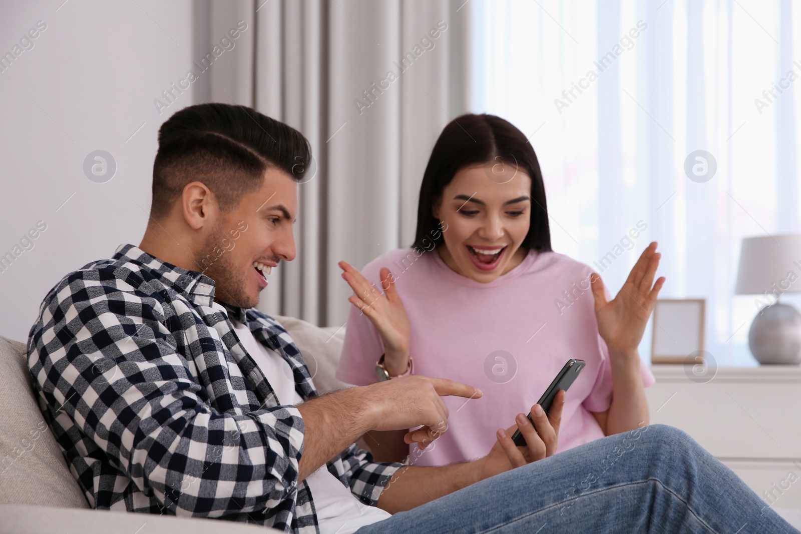 Photo of Emotional couple participating in online auction using smartphone at home