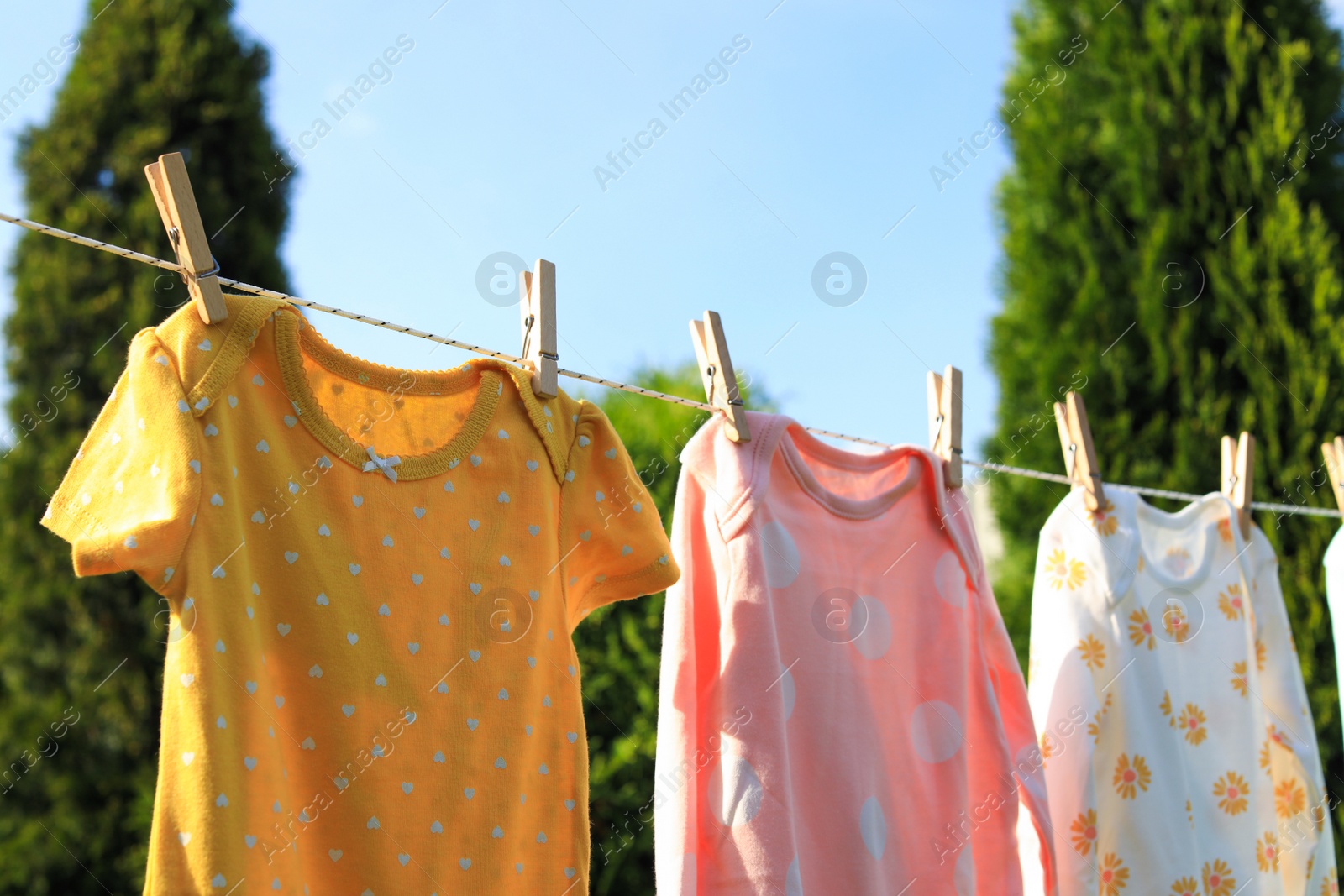 Photo of Clean baby onesies hanging on washing line in garden. Drying clothes