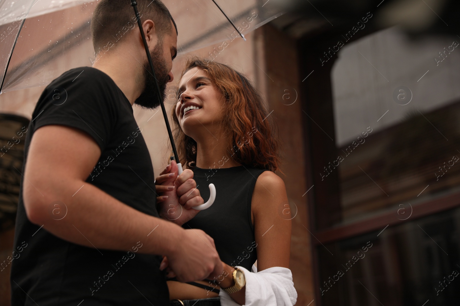 Photo of Young couple with umbrella enjoying time together under rain on city street, space for text