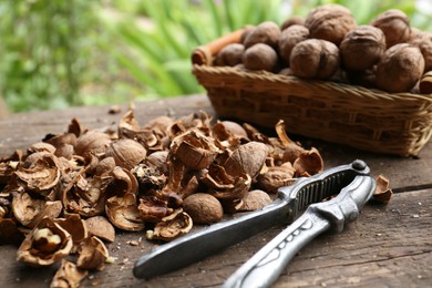 Photo of Walnuts, pieces of shells and nutcracker on wooden table against blurred background
