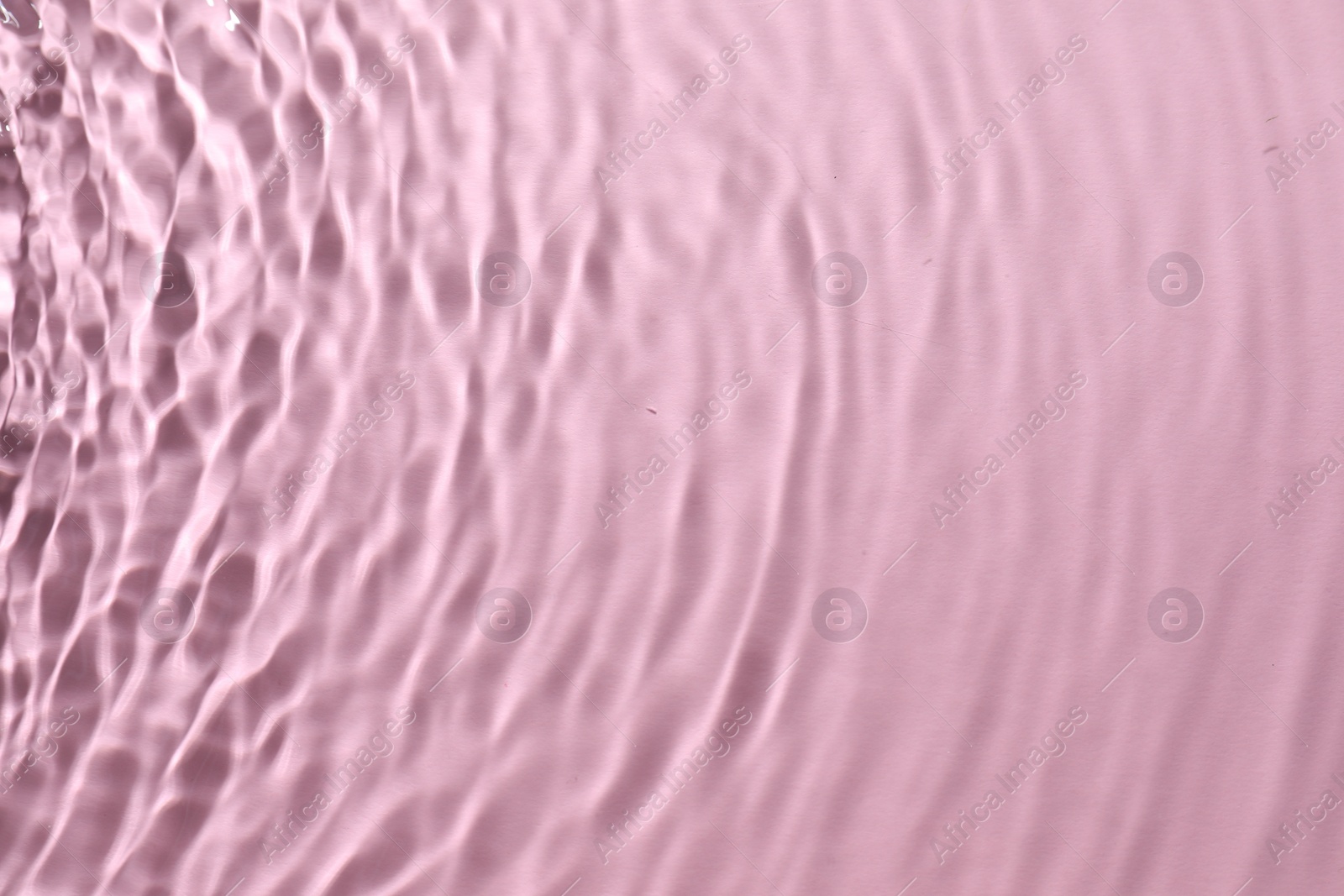 Photo of Rippled surface of clear water on pink background, top view