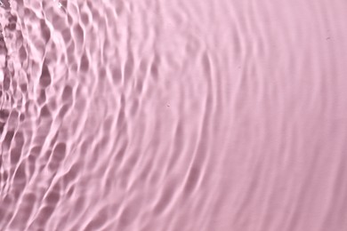 Rippled surface of clear water on pink background, top view