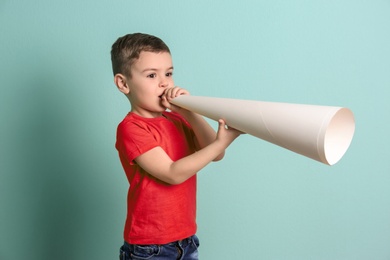 Adorable little boy with paper megaphone on color background