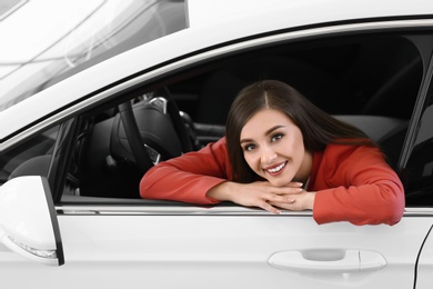 Photo of Young woman sitting in driver's seat of new car at salon