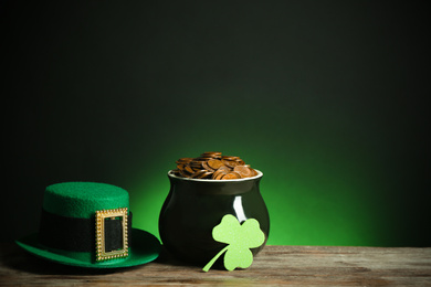 Photo of Pot with gold coins, hat and clover on wooden table against dark background, space for text. St. Patrick's Day