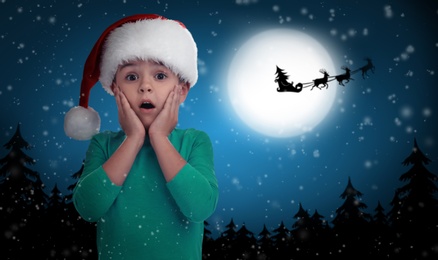 Image of Cute little child and Santa Claus flying in his sleigh against moon sky on background. Christmas celebration